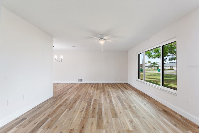 spare room with ceiling fan with notable chandelier and light wood-type flooring