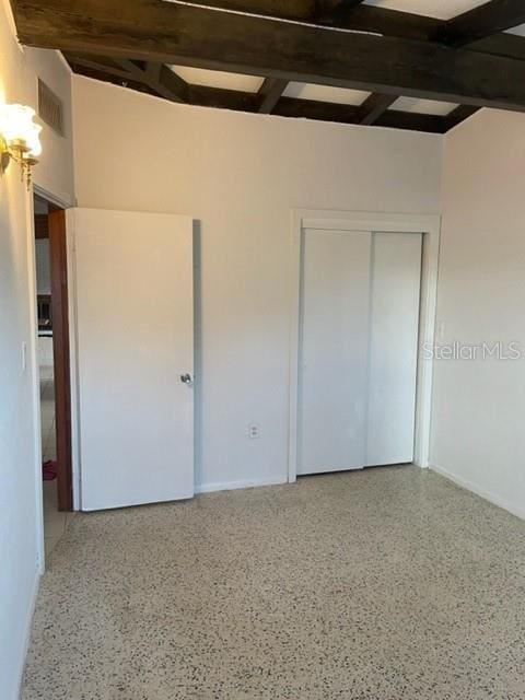 unfurnished bedroom featuring speckled floor, visible vents, baseboards, a closet, and beam ceiling