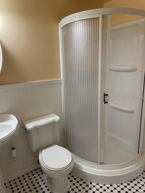 full bathroom featuring toilet, tile patterned floors, a shower stall, and wainscoting