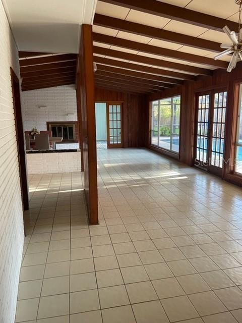 unfurnished room with vaulted ceiling with beams, wood walls, light tile patterned flooring, and french doors