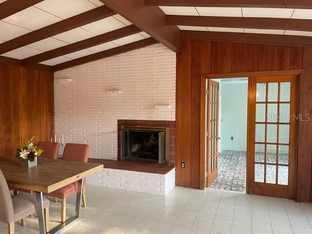 unfurnished living room featuring vaulted ceiling with beams, wood walls, and a brick fireplace