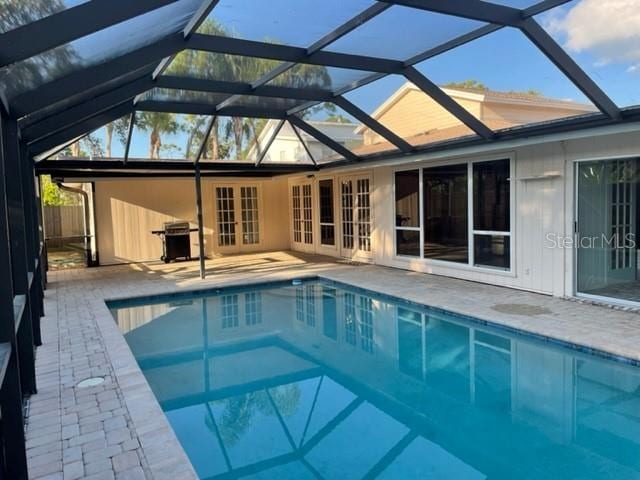 outdoor pool featuring glass enclosure, a patio area, grilling area, and french doors