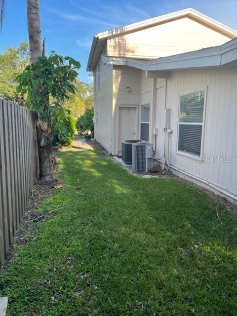 view of side of home featuring cooling unit, a lawn, and fence