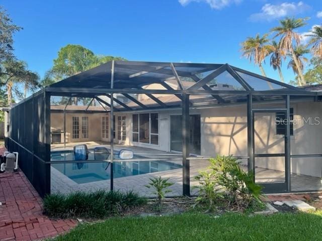 back of house featuring glass enclosure, a patio, and an outdoor pool