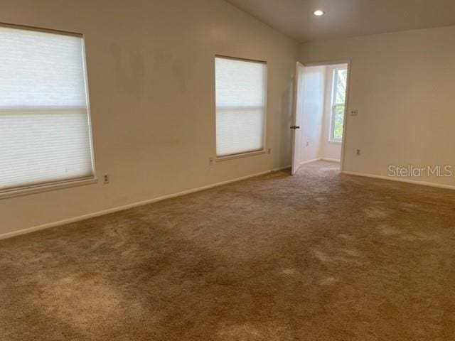 spare room with dark carpet, recessed lighting, vaulted ceiling, and baseboards