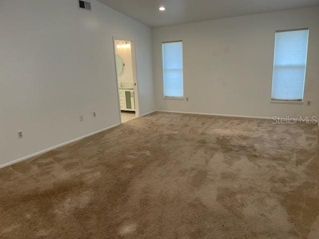 spare room with carpet flooring, vaulted ceiling, visible vents, and baseboards