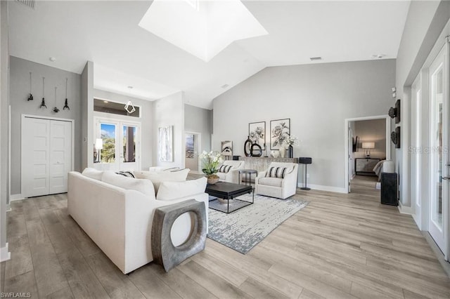 living room with french doors, high vaulted ceiling, a skylight, and light hardwood / wood-style floors