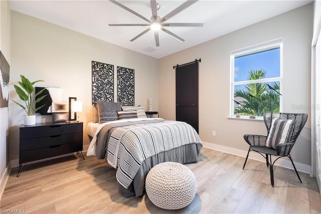 bedroom with light hardwood / wood-style floors, a barn door, and ceiling fan