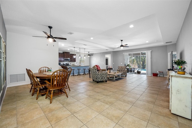 dining space with ceiling fan, a raised ceiling, and light tile patterned floors