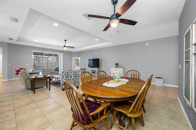 tiled dining space with ceiling fan and a tray ceiling