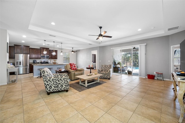 living room with a raised ceiling, ceiling fan, and light tile patterned flooring