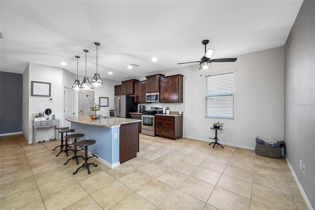 kitchen with appliances with stainless steel finishes, an island with sink, a breakfast bar area, light stone counters, and dark brown cabinets