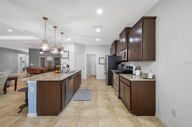 kitchen featuring appliances with stainless steel finishes, an island with sink, sink, hanging light fixtures, and light stone countertops