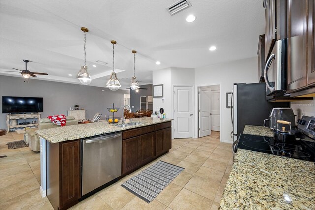 kitchen featuring an island with sink, sink, hanging light fixtures, stainless steel appliances, and light stone countertops