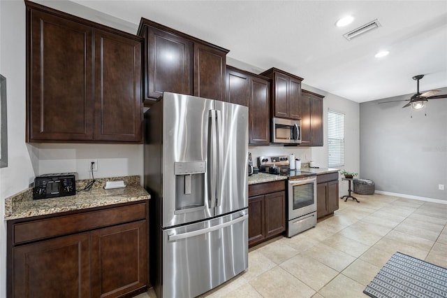 kitchen featuring dark brown cabinets, light tile patterned floors, ceiling fan, stainless steel appliances, and light stone countertops