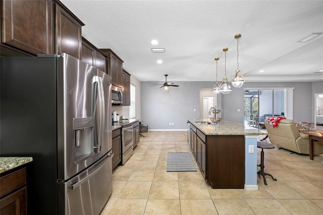 kitchen with stainless steel appliances, light stone countertops, sink, and a center island with sink