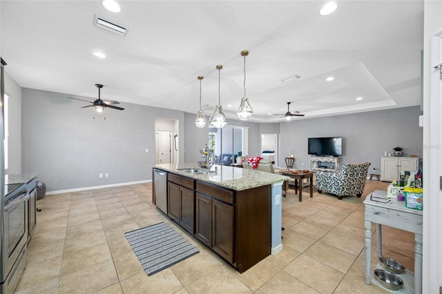 kitchen featuring sink, light stone counters, pendant lighting, stainless steel appliances, and a kitchen island with sink