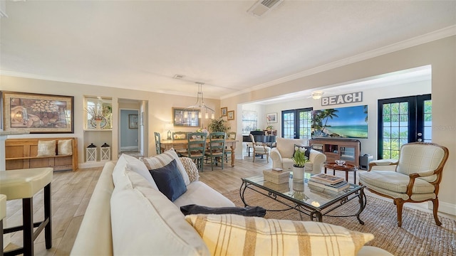 living room with a notable chandelier, crown molding, french doors, and light wood-type flooring