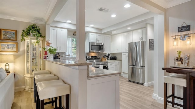 kitchen with a breakfast bar area, stainless steel appliances, light stone countertops, white cabinets, and kitchen peninsula