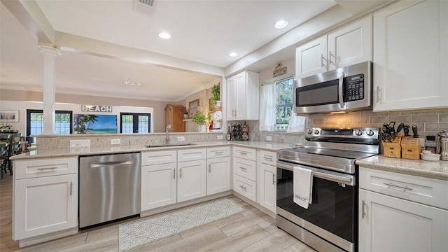 kitchen with sink, white cabinets, light stone counters, kitchen peninsula, and stainless steel appliances