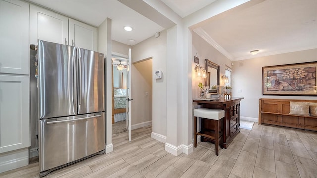 kitchen with white cabinetry, stainless steel fridge, and crown molding