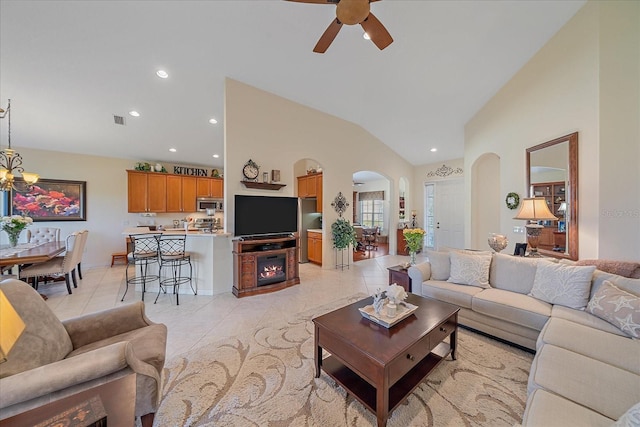 tiled living room with ceiling fan with notable chandelier and high vaulted ceiling