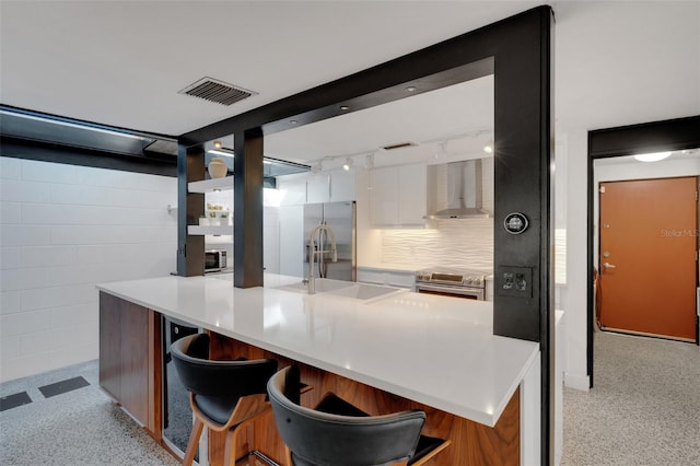 kitchen featuring white cabinetry, sink, a kitchen island with sink, and wall chimney range hood