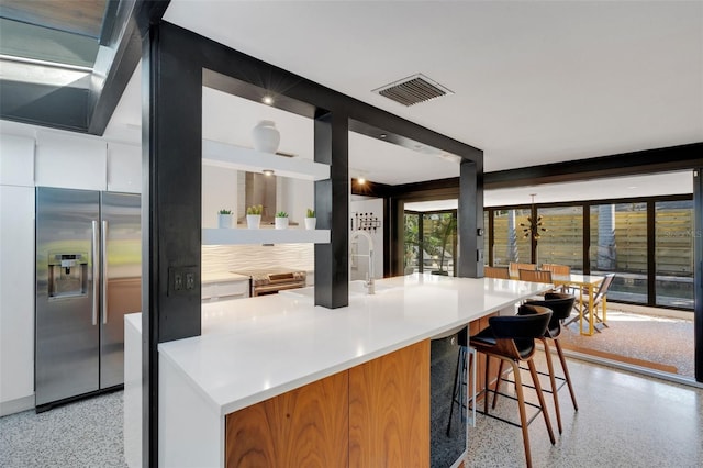 kitchen featuring a kitchen island with sink, a breakfast bar area, and stainless steel fridge