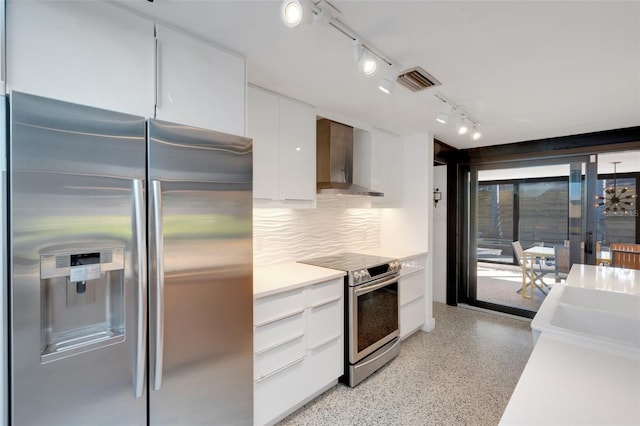 kitchen featuring white cabinets, decorative backsplash, stainless steel appliances, track lighting, and wall chimney exhaust hood