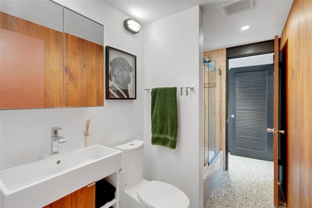 bathroom featuring a shower with door, sink, and toilet