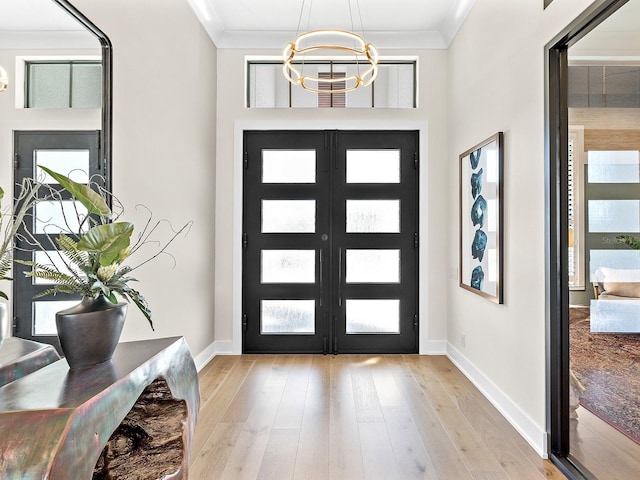 entrance foyer with light wood finished floors, baseboards, ornamental molding, and a notable chandelier