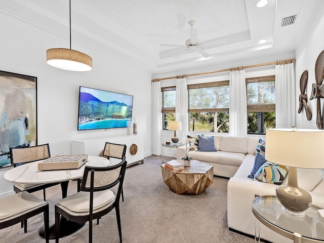 living area with a tray ceiling, light colored carpet, visible vents, a ceiling fan, and baseboards