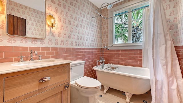 full bath with wallpapered walls, wainscoting, a soaking tub, vanity, and tile walls