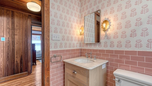 bathroom featuring toilet, a wainscoted wall, tile walls, vanity, and wallpapered walls