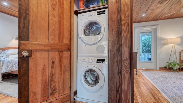 laundry area with wooden ceiling, stacked washing maching and dryer, laundry area, and wood finished floors