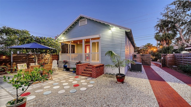 view of front of property featuring a porch, cooling unit, fence, and a patio