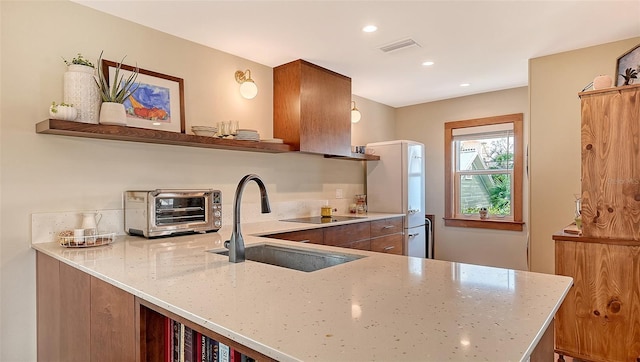 kitchen with visible vents, light stone counters, a sink, and freestanding refrigerator