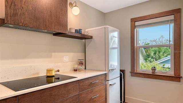 kitchen with black electric stovetop, freestanding refrigerator, light stone countertops, open shelves, and modern cabinets