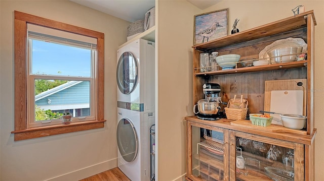 clothes washing area with baseboards, stacked washing maching and dryer, and wood finished floors