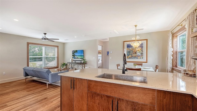 kitchen featuring light stone counters, light wood-type flooring, brown cabinetry, and a sink