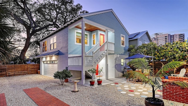 back of property featuring gravel driveway, an attached garage, a patio area, fence, and stairs