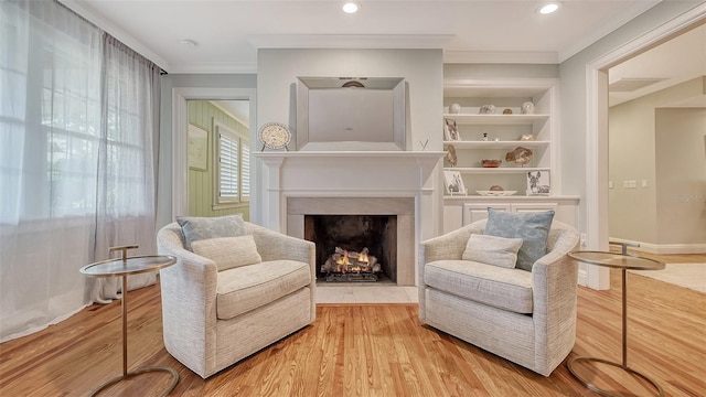 sitting room with crown molding, built in features, and light wood-type flooring