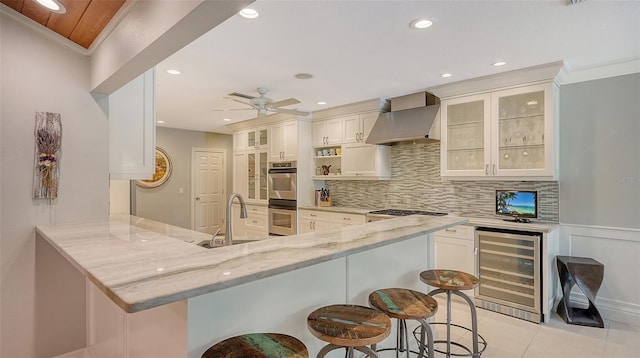 kitchen featuring sink, a breakfast bar area, beverage cooler, kitchen peninsula, and wall chimney range hood