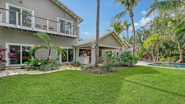 rear view of property featuring a balcony and a yard