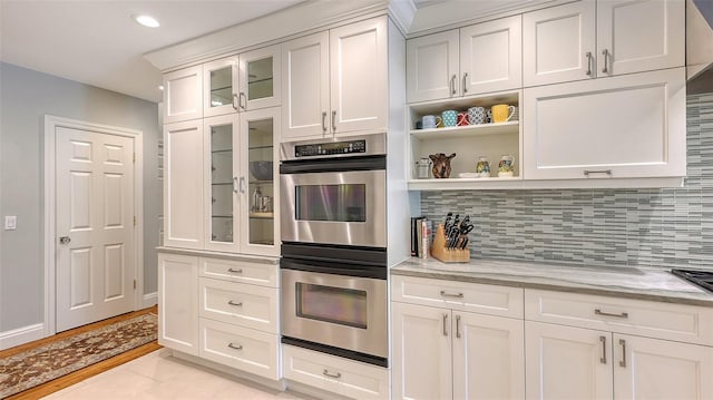 kitchen with light tile patterned floors, light stone counters, white cabinets, decorative backsplash, and stainless steel double oven