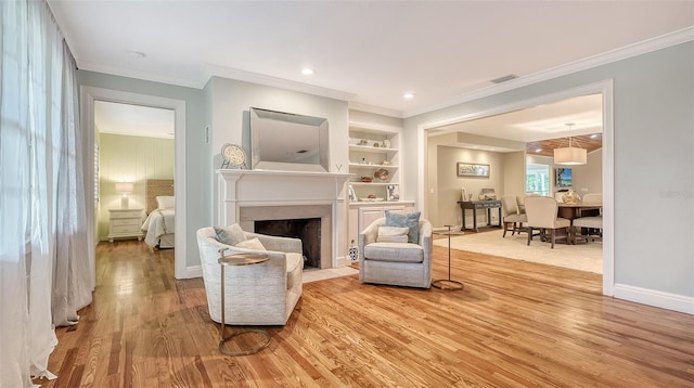 living area featuring crown molding, built in shelves, and light hardwood / wood-style floors