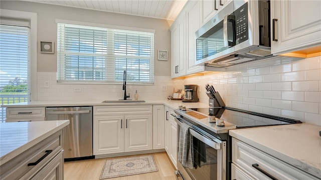 kitchen with stainless steel appliances, white cabinetry, sink, and light hardwood / wood-style floors