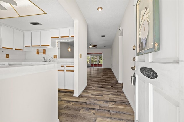 kitchen featuring white cabinetry, tile counters, backsplash, ceiling fan, and dark wood-type flooring