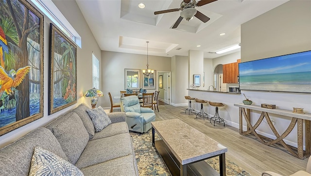 living room featuring ceiling fan with notable chandelier, a raised ceiling, and light hardwood / wood-style floors