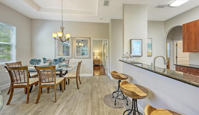 dining area featuring sink, a tray ceiling, light hardwood / wood-style floors, and a chandelier